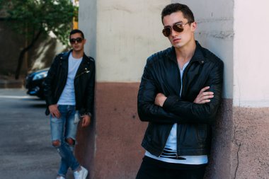 güzel ve çekici adam şehirde ayakta, poz. bir siyah deri ceket, beyaz T-shirt, kot pantolon ve beyaz ayakkabı giymiş. ayna Binası yakınında. siyah gözlük şehirde dolaşmak. iletişim. Toplantı arkadaşlar.