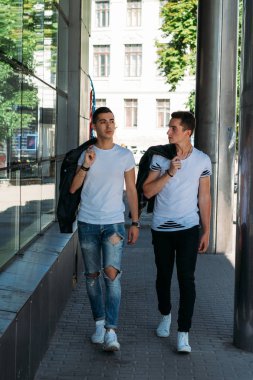 güzel ve çekici adam şehirde ayakta, poz. bir siyah deri ceket, beyaz T-shirt, kot pantolon ve beyaz ayakkabı giymiş. ayna Binası yakınında. siyah gözlük şehirde dolaşmak. iletişim. Toplantı arkadaşlar.