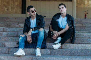 güzel ve çekici adam şehirde ayakta, poz. bir siyah deri ceket, beyaz T-shirt, kot pantolon ve beyaz ayakkabı giymiş. ayna Binası yakınında. siyah gözlük şehirde dolaşmak. iletişim. Toplantı arkadaşlar.