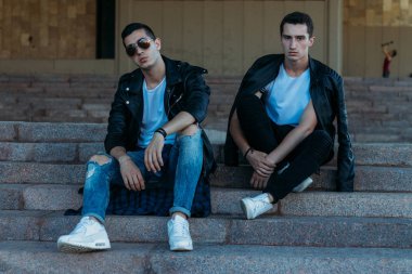 güzel ve çekici adam şehirde ayakta, poz. bir siyah deri ceket, beyaz T-shirt, kot pantolon ve beyaz ayakkabı giymiş. ayna Binası yakınında. siyah gözlük şehirde dolaşmak. iletişim. Toplantı arkadaşlar.