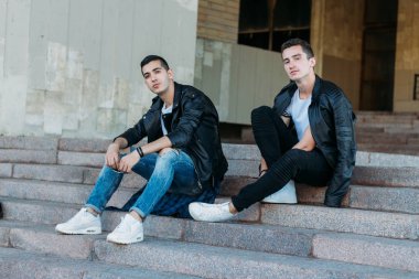 güzel ve çekici adam şehirde ayakta, poz. bir siyah deri ceket, beyaz T-shirt, kot pantolon ve beyaz ayakkabı giymiş. ayna Binası yakınında. siyah gözlük şehirde dolaşmak. iletişim. Toplantı arkadaşlar.