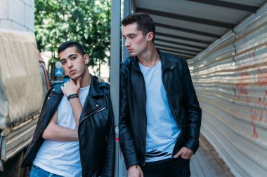 güzel ve çekici adam şehirde ayakta, poz. bir siyah deri ceket, beyaz T-shirt, kot pantolon ve beyaz ayakkabı giymiş. ayna Binası yakınında. şehir etrafında yürümek. iletişim. Toplantı arkadaşlar.