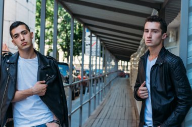 güzel ve çekici adam şehirde ayakta, poz. bir siyah deri ceket, beyaz T-shirt, kot pantolon ve beyaz ayakkabı giymiş. ayna Binası yakınında. şehir etrafında yürümek. iletişim. Toplantı arkadaşlar.