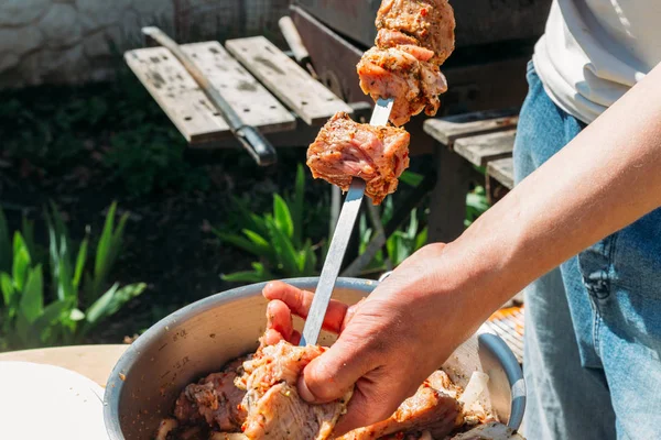 一个人把生肉串在金属烤肉串上 放在火上煮 烤小鱼烤肉串 串上的肉放在一个白色的托盘上 用洋葱和辣椒煮肉 — 图库照片