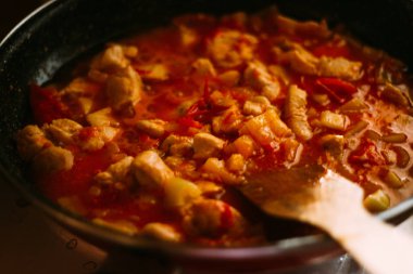 tahta bir spatula ile karıştırın, yemek. Ocakta bir tavada domates soslu tavuk ile vardır. Bir yemek hazırlamak