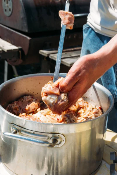 Человек нанизывает кусочки сырого мяса на металлический шампур, чтобы приготовить его на огне. барбекю. варить мясо с луком и перцем . — стоковое фото