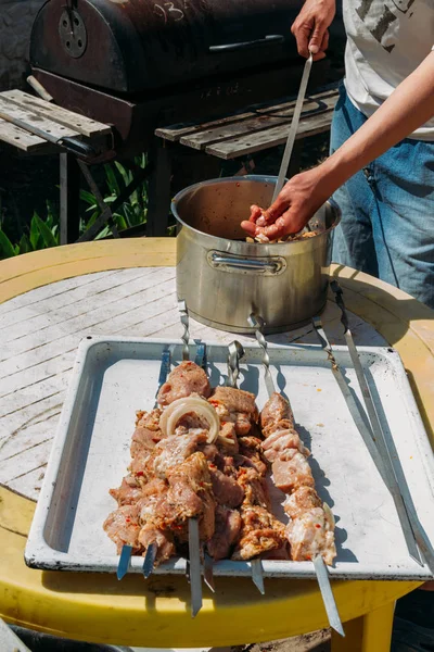 bir adam için ateşe cook metal bir şiş üzerinde çiğ et parçalarını dizeleri. Barbekü. soğan ve biber et pişirmek.