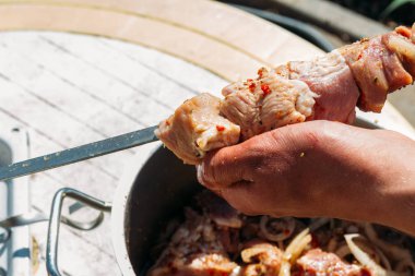 bir adam için ateşe cook metal bir şiş üzerinde çiğ et parçalarını dizeleri. Barbekü. soğan ve biber et pişirmek.