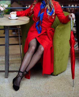 kırmızı bir yağmurluk File Taytlı kız bir fincan kahve bir kafede oturuyor, yanında öyle bir toplantı için bekleyen bir kırmızı şemsiye