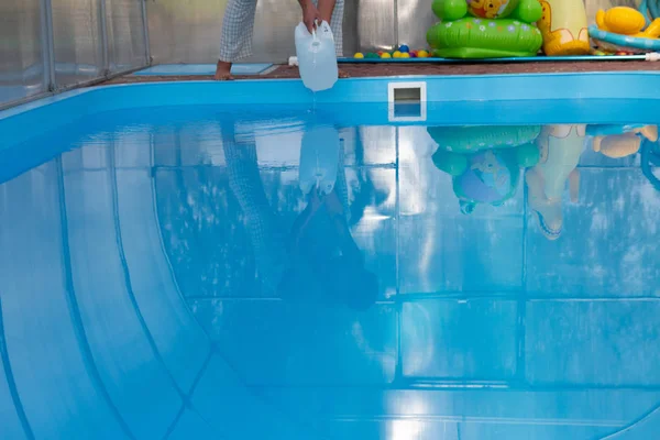 Las manos de los hombres vierten líquido claro de un tanque de plástico en una piscina, en el agua. purificación química del agua, equilibrio alcalino, condiciones insalubres. desinfección y preparación para nadar. el cuidado de la p —  Fotos de Stock