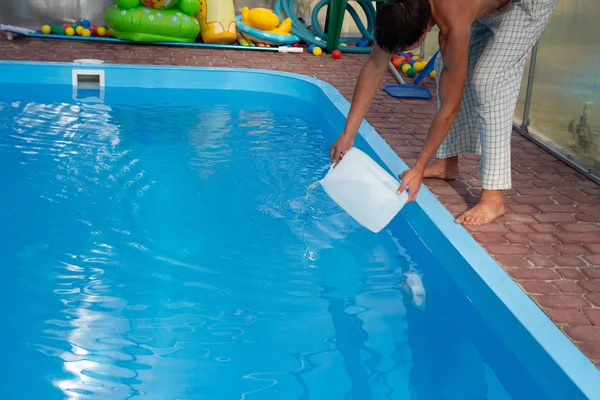 Les mains des hommes versent le liquide léger d'un réservoir en plastique dans une piscine, dans l'eau. purification chimique de l'eau, équilibre alcalin, conditions insalubres. désinfection et préparation à la baignade. soins pour le p — Photo