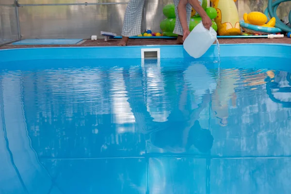 Las manos de los hombres vierten líquido claro de un tanque de plástico en una piscina, en el agua. purificación química del agua, equilibrio alcalino, condiciones insalubres. desinfección y preparación para nadar. el cuidado de la p —  Fotos de Stock