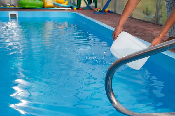 Las manos de los hombres vierten líquido claro de un tanque de plástico en una piscina, en el agua. purificación química del agua, equilibrio alcalino, condiciones insalubres. desinfección y preparación para nadar. el cuidado de la p —  Fotos de Stock