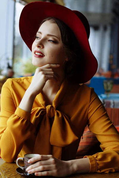 Bir kafede bir kız portresi ile bir fincan kahve ve bir hat.portrait şehvetli genç kızın disket şapka ve yay ile bluz giyiyor. Kafede kahve tutan güzel esmer kadın — Stok fotoğraf