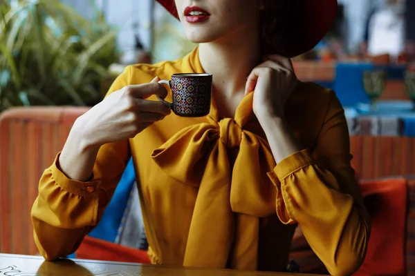 Portrait d'une fille dans un café avec une tasse de café et un chapeau.portrait d'une jeune fille sensuelle portant un chapeau disquette et une blouse avec arc. Belle femme brune dans un café tenant une tasse de café — Photo