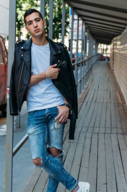 yakışıklı, çekici bir adam, ayakta beyaz bir T-shirt, Korkuluk üzerine eğilerek siyah, deri ceket, siyah pantolon ve beyaz spor ayakkabı, mokasen, sketchboards,