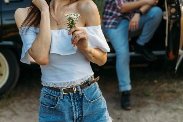 Ein Mädchen mit einer Blume und einer weißen Bluse, ein Mann im karierten Hemd sitzt auf der Rückseite des Autositzes und wartet Stockbild