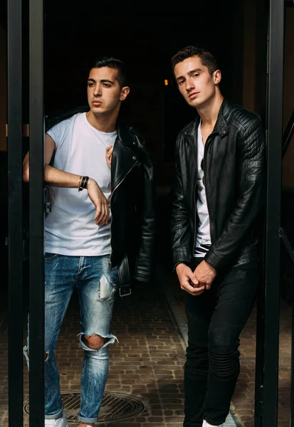 two attractive men are standing nearby, friends, posing, in black jackets and white T-shirts