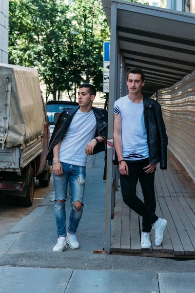 Dos hombres atractivos están de pie cerca, amigos, posando, en chaquetas negras y camisetas blancas — Foto de Stock