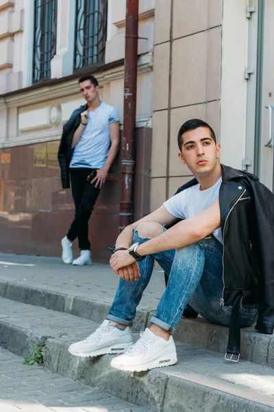 two attractive men are standing nearby, friends, posing, in black jackets and white T-shirts