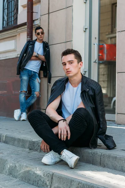 Twee aantrekkelijke mannen staan in de buurt, vrienden, poseren, in zwarte jassen en witte T-shirts — Stockfoto