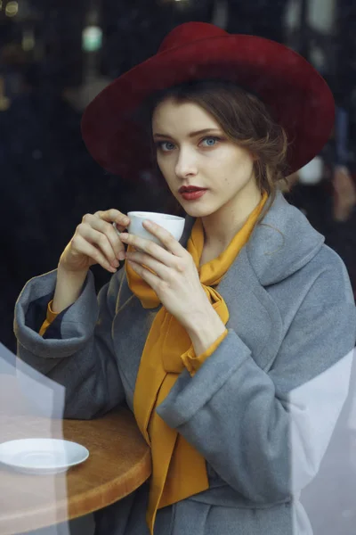 girl in a cafe with a cup of coffee and a hat.portrait of sensual young girl wearing floppy hat and blouse with bow. Beautiful brunette woman in cafe holding cup of coffee