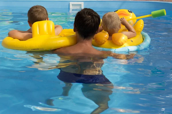 Ein Mann schwimmt in einem Pool mit zwei Kindern in gelben aufblasbaren Kreisen — Stockfoto