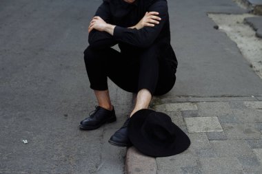 siyah bir şapka ile siyah bir adam asfalt yolda sokakta oturuyor.