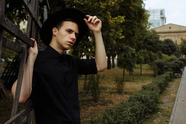 Du är välkommen koncept. en kille i en svart skjorta, nära ett träs taket, höjde sin hand till sin hatt, Cowboy. Hälsning. — Stockfoto