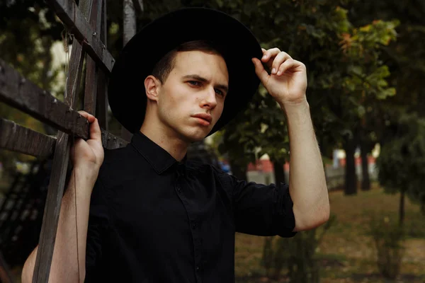 You are welcome concept. a guy in a black shirt, near a wooden fence, raised his hand to his hat, cowboy. greeting.