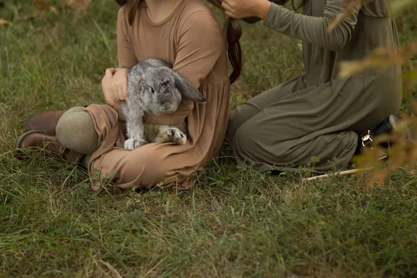 a gray rabbit is sleeping in the arms of a girl sitting on the grass.