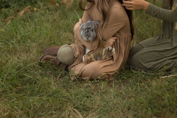 a gray rabbit is sleeping in the arms of a girl sitting on the grass.