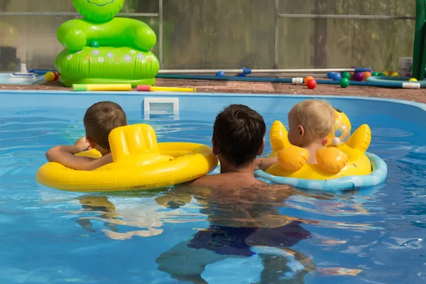 Zwei Kinder mit Trainer, mit Papa schwimmen lernen im Pool, Rückansicht. Sorgen, Urlaub. aufblasbare Kreise. Rettungsring — Stockfoto