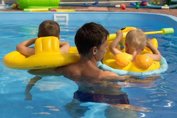 Двое детей с тренером, с папой учатся плавать в бассейне, вид сзади. заботы, отпуск. надувные круги. Лайфбуй — стоковое фото