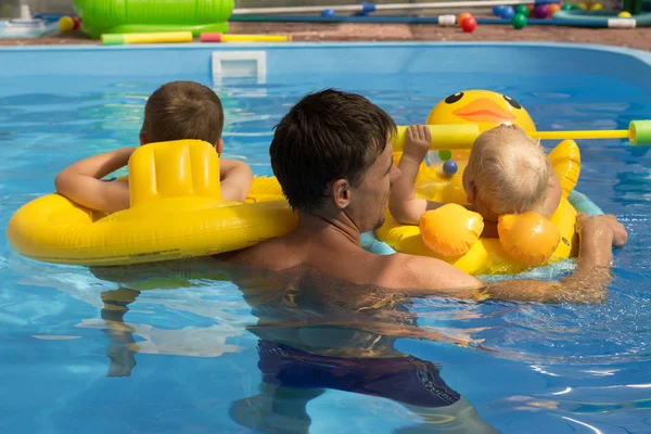 Zwei Kinder mit Trainer, mit Papa schwimmen lernen im Pool, Rückansicht. Sorgen, Urlaub. aufblasbare Kreise. Rettungsring — Stockfoto