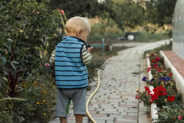 Egy kis gyermek sétál végig egy ösvényen egy virágágyás, azt vizsgálja, virágok — Stock Fotó