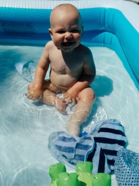 küçük bir çocuk havuzda oturur ve gülümsüyor, oynar, güneş yaz parlar