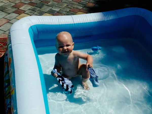 Malé dítě sedí v bazénu a usmívá se, slunce září v létě — Stock fotografie