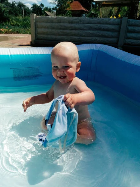 Ein kleines kind sitzt im pool und lächelt, spielt, die sonne scheint sommer — Stockfoto