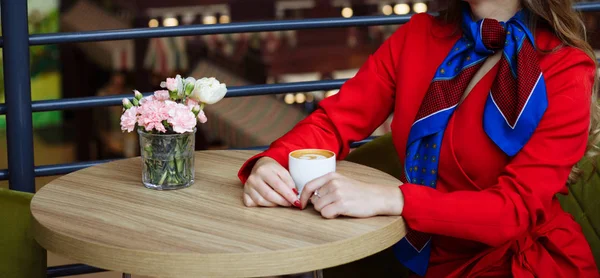 Дівчина в червоному плащі в ажурних колготках, сидить в кафе над чашкою кави, чекаючи на зустріч — стокове фото