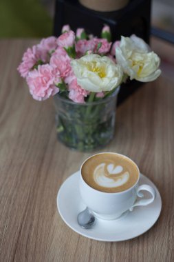 Ahşap masa arkasında bir fincan sıcak latte sanat kahvesi.