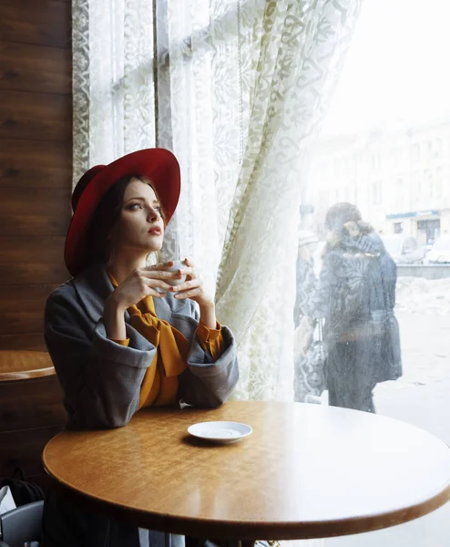 Дівчина в кафе з чашкою кави і капелюхом.портрет чуттєвої молодої дівчини в капелюсі та блузці з бантом. Красива брюнетка в кафе тримає чашку кави — стокове фото