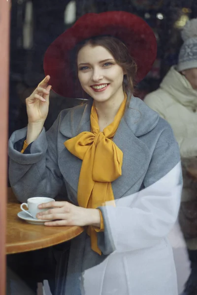 Fille dans un café avec une tasse de café et un chapeau.portrait de la jeune fille sensuelle portant un chapeau disquette et chemisier avec arc. Belle femme brune dans un café tenant une tasse de café — Photo