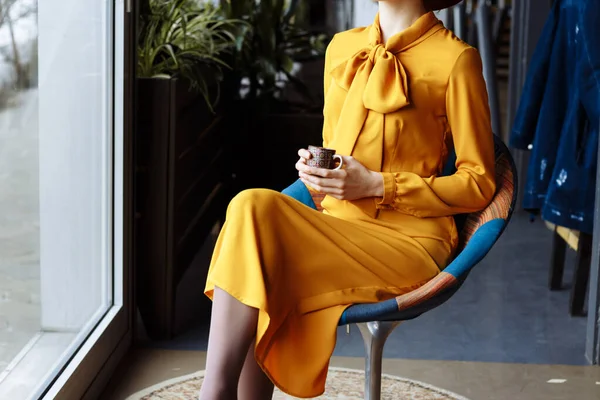 Meisje in een café met een kop koffie en een hoed.portret van sensueel jong meisje met een slappe hoed en blouse met strik. Mooie brunette vrouw in cafe holding kopje koffie — Stockfoto