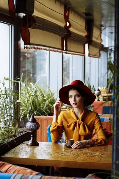 コーヒーと帽子をかぶったカフェの女の子。フロッピーハットを被った官能的な若い女の子の肖像画と弓でブラウス。美しいですブルネット女性でカフェ開催カップのコーヒー — ストック写真
