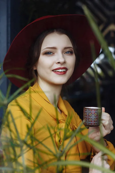 Kafede bir fincan kahve ve şapkalı bir kız. Sarkık şapkalı ve fiyonklu bluz giyen şehvetli bir genç kızın portresi. Kafede elinde kahve tutan güzel esmer kadın. — Stok fotoğraf