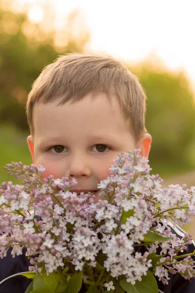 Portret van een jongen met lila. boeket paarse lila in kinderhanden. handen met een paarse lila bloemen boeket in weide. — Stockfoto