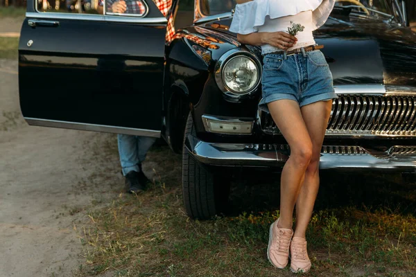 Ein Mädchen mit einer Blume und einer weißen Bluse, ein Mann im karierten Hemd sitzt auf der Rückseite des Autositzes und wartet — Stockfoto