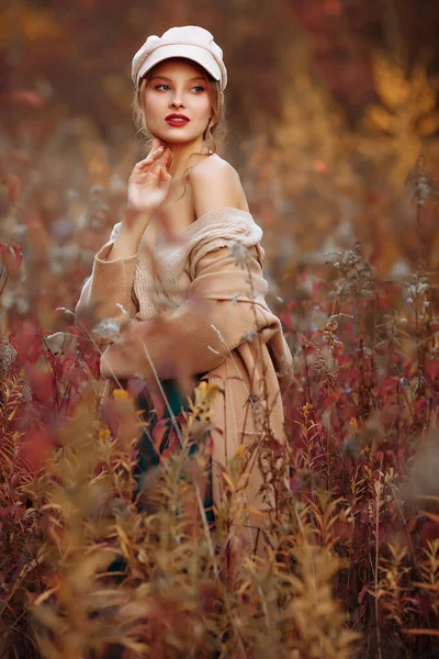 Piękna dziewczyna w czapce i płaszczu z gołym ramieniem na tle jesieni — Zdjęcie stockowe