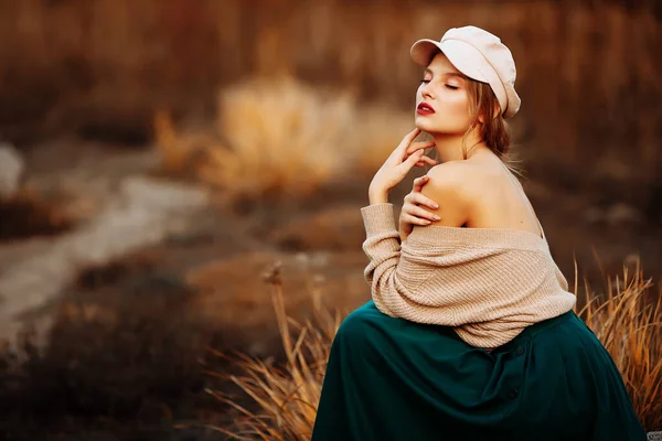 Hermosa chica en una gorra y un abrigo con un hombro desnudo en el fondo del otoño — Foto de Stock